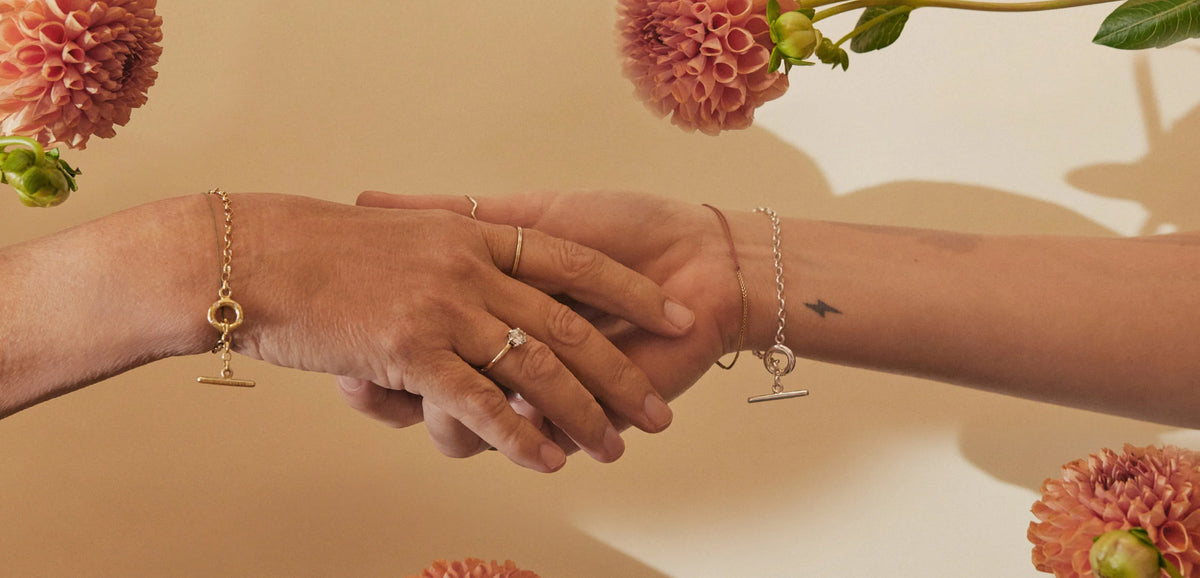 Two hands holding each other with Famke jewellery and flowers in the background